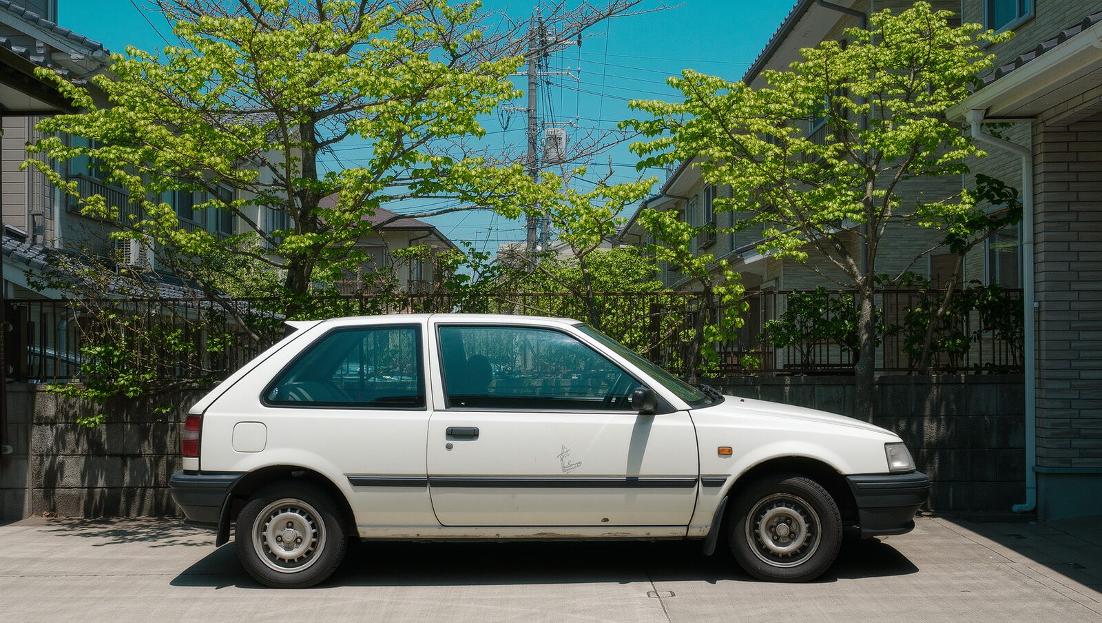 新緑の住宅街の駐車場に停まる年式の古い白い車
